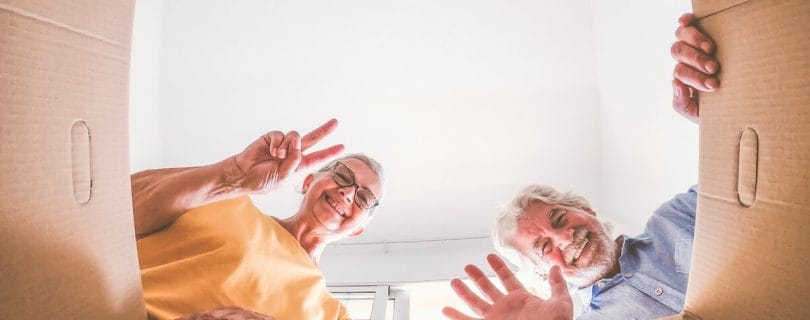 Smiling older adults waving hello from a cardboard box