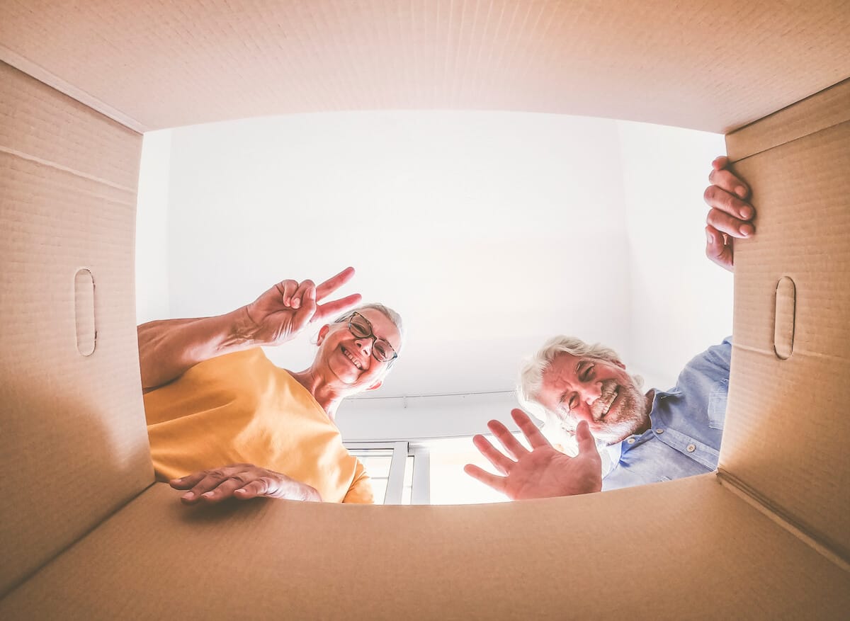 Smiling older adults waving hello from a cardboard box